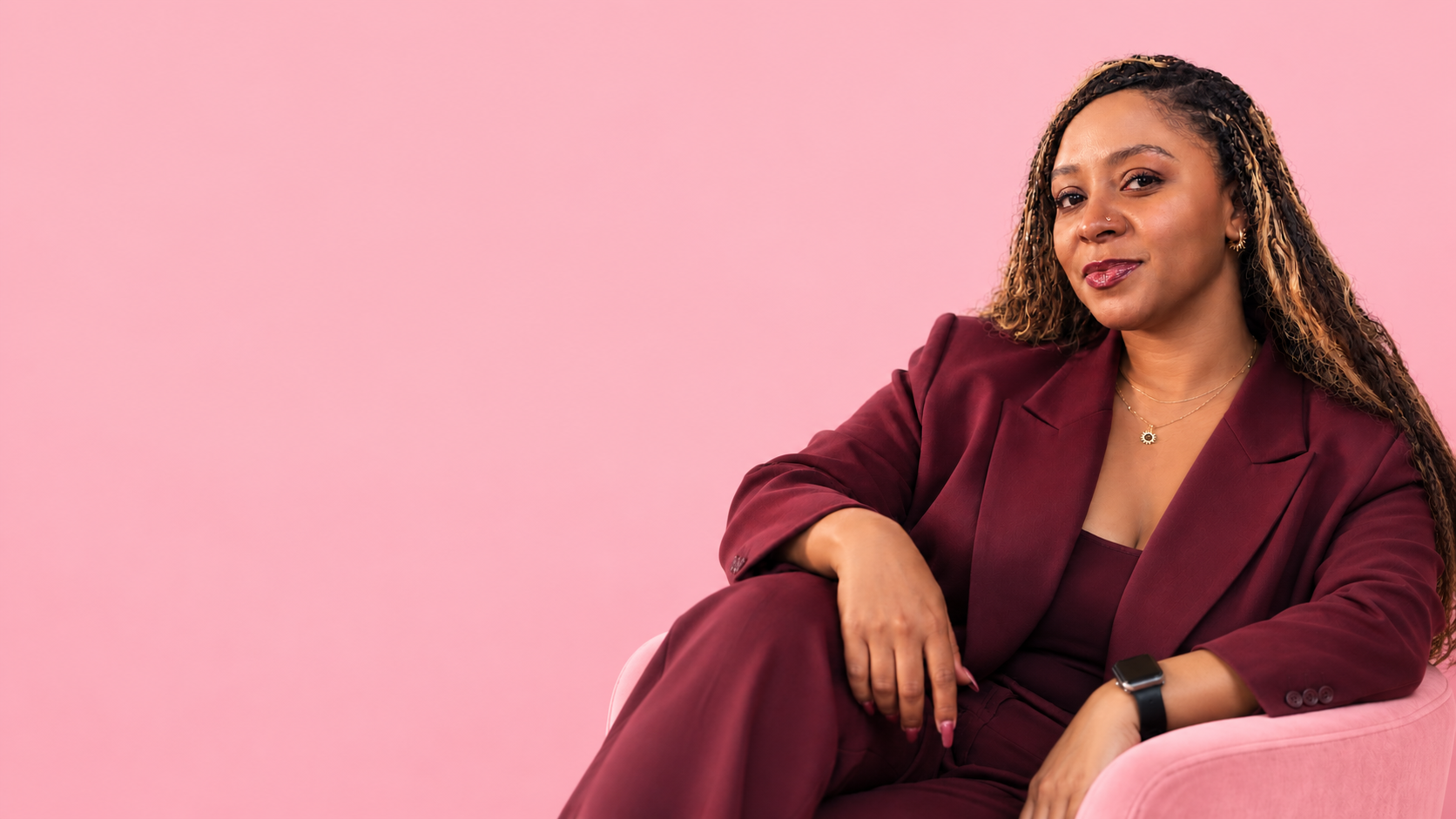 Jaliyah Jasper, founder of JJasper+Co., seated in a pink chair wearing a burgundy suit